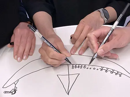 vier Hände zeichnen gemeinsam ein Segelschiff im Team-Workshop 